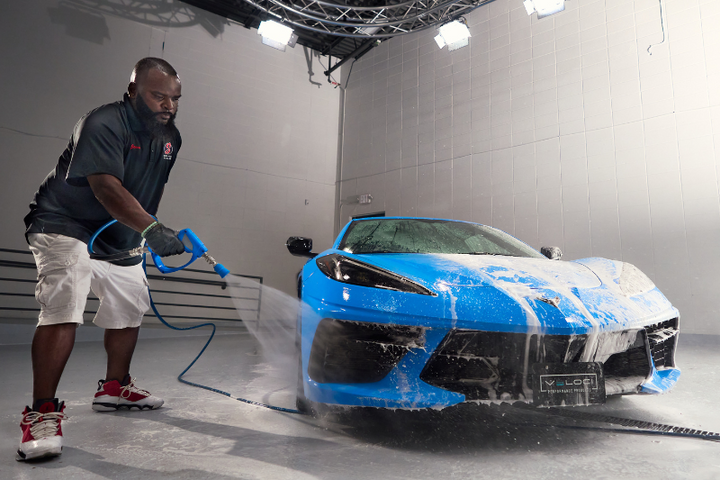 a man spraying a blue car with pressure washer